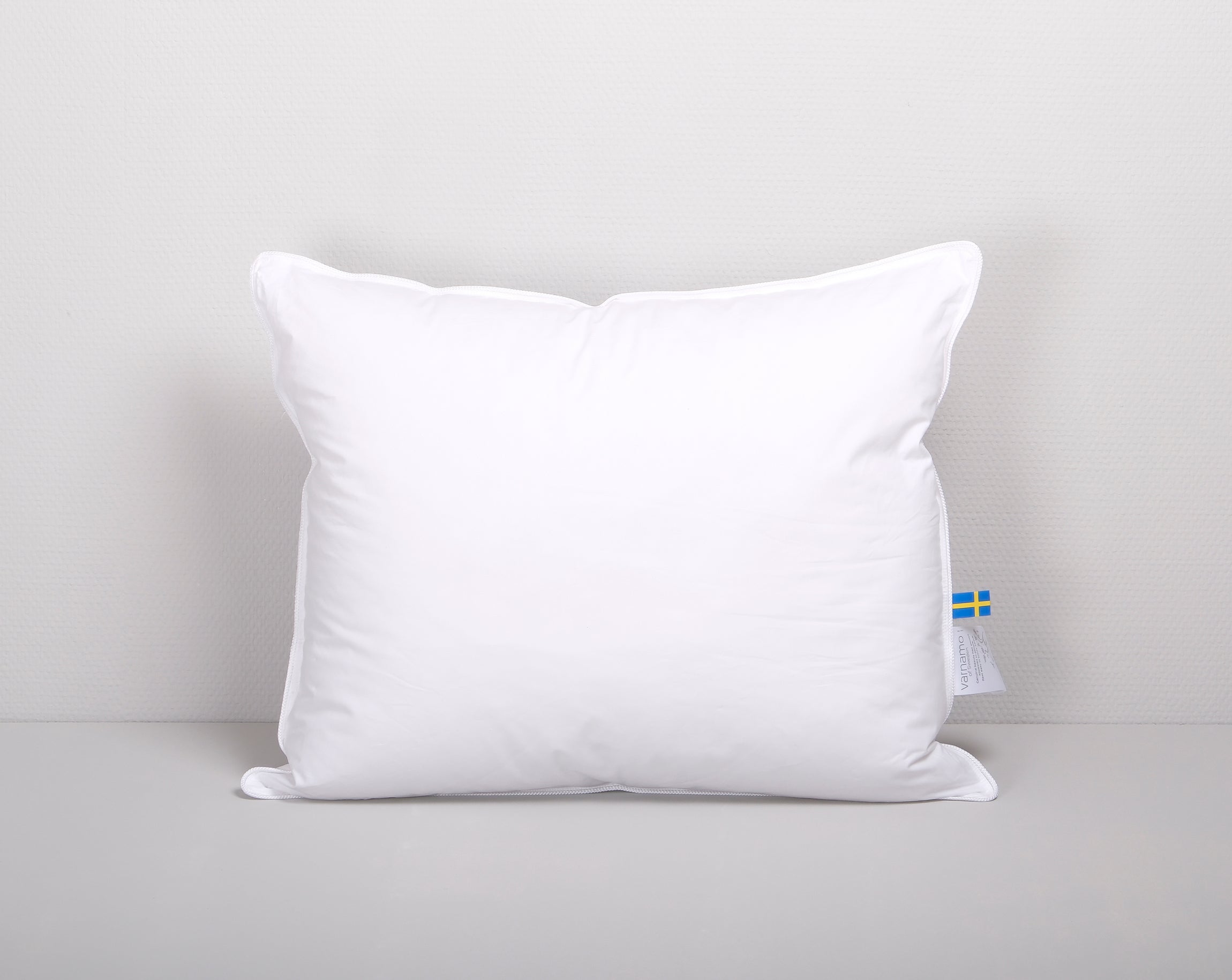 Vit rektangulär kudde mot en ljusgrå bakgrund.