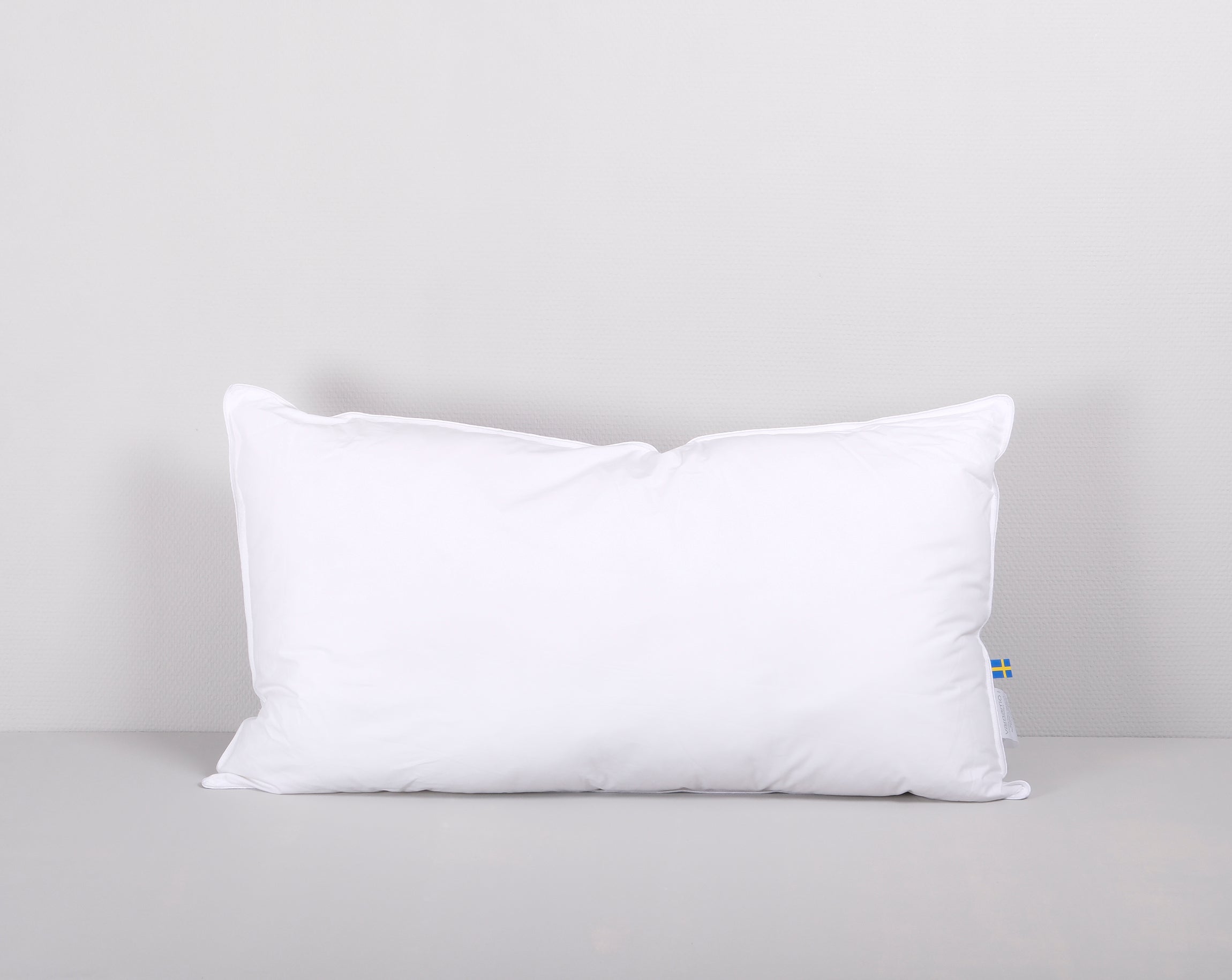 Vit lång kudde mot en ljusgrå bakgrund.